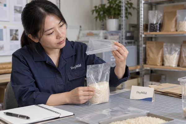 Asian sample reviewer inspecting DayMild kitchen trash bags: bin-rim fit, bottom-seam integrity and usable roll count